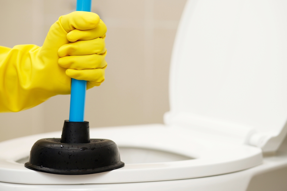 Serviceman repairing toilet with hand plunger. Clogged toilet.